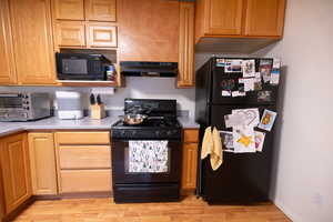 Kitchen featuring black appliances, light countertops, light wood-style flooring, under cabinet range hood, and brown cabinetry