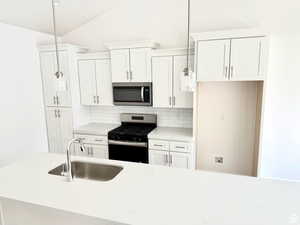 Kitchen with appliances with stainless steel finishes, light stone countertops, white cabinets, tasteful backsplash, and vaulted ceiling