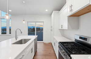 Kitchen featuring stainless steel appliances, white cabinetry, pendant lighting, light wood-type flooring, and light stone counters