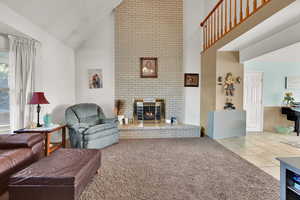 Living area featuring light tile patterned floors, light colored carpet, high vaulted ceiling, and a brick fireplace