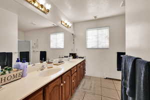 Bathroom with double vanity, light tile patterned floors, a textured ceiling, baseboard heating, and a shower with door