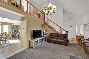 Living room featuring light tile patterned floors, high vaulted ceiling, light colored carpet, a chandelier, and stairway