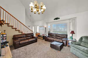 Carpeted living area featuring high vaulted ceiling, a chandelier, and stairway