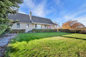 Rear view of property featuring a chimney, a lawn, a shingled roof, and brick siding