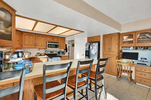 Kitchen with a kitchen breakfast bar, a peninsula, brown cabinets, light tile patterned floors, and stainless steel appliances