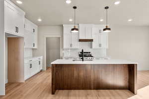Kitchen with hanging light fixtures, recessed lighting, white cabinetry, a center island with sink, and light stone counters