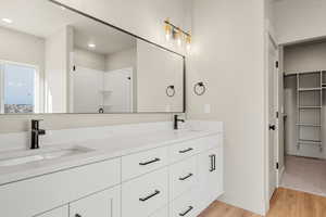 Full bath with light wood-type flooring, a stall shower, double vanity, a spacious closet, and recessed lighting