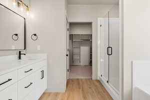 Full bathroom with a spacious closet, light wood finished floors, vanity, and a stall shower
