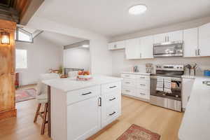 Kitchen featuring stainless steel appliances, a kitchen breakfast bar, light wood finished floors, white cabinets, and a center island