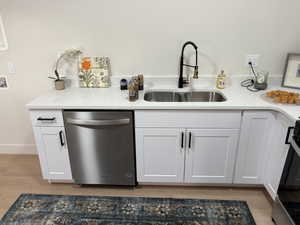 Kitchen featuring white cabinetry, dishwasher, light stone counters, light wood-type flooring, and range