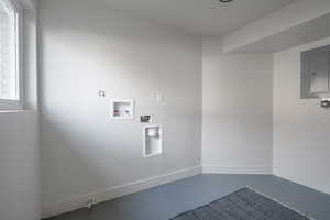 Washroom featuring concrete flooring, electric panel, and hookup for a washing machine