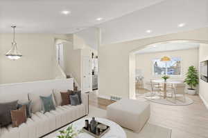 Living area with arched walkways, light wood-style floors, vaulted ceiling, recessed lighting, and stairs