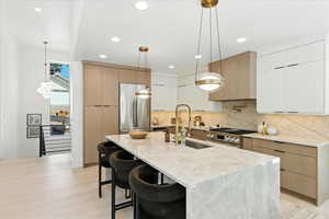 Kitchen featuring modern cabinets, light stone countertops, stainless steel appliances, hanging light fixtures, and a kitchen bar