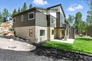 Rear view of house featuring stone siding, a patio area, board and batten siding, stairway, and a yard