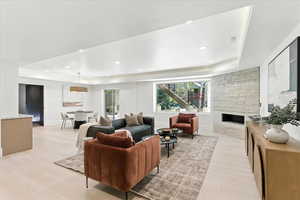 Living room featuring a tray ceiling, a stone fireplace, recessed lighting, and light wood-style floors