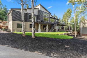 Back of property featuring a patio, stone siding, a deck, board and batten siding, and a yard
