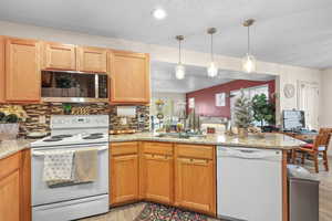 Kitchen with white appliances, a textured ceiling, a peninsula, pendant lighting, and light stone counters