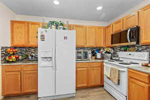 Kitchen featuring white appliances, light stone countertops, tasteful backsplash, light wood-type flooring, and recessed lighting