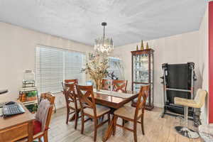 Dining space with a textured ceiling, light wood-type flooring, a chandelier, and a desk