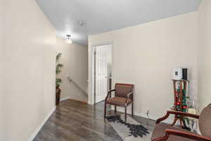 Sitting room with an upstairs landing, dark wood-style floors, and a textured ceiling