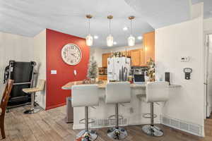 Kitchen featuring a breakfast bar area, light wood-style flooring, a peninsula, pendant lighting, and white fridge with ice dispenser