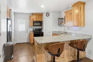 Kitchen with light stone countertops, open shelves, a peninsula, dark wood-style flooring, and a kitchen bar