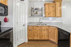 Kitchen with black appliances, open shelves, light wood-type flooring, light stone countertops, and light brown cabinetry