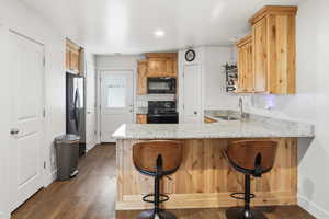 Kitchen with light stone counters, a breakfast bar area, black appliances, a peninsula, and dark wood-style flooring
