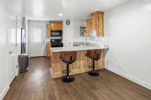 Kitchen featuring a kitchen breakfast bar, black appliances, light stone counters, a peninsula, and dark wood finished floors