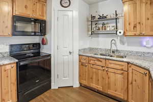 Kitchen featuring black appliances, dark wood finished floors, and light stone countertops