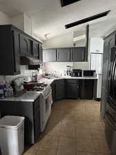 Kitchen featuring lofted ceiling, white range with gas cooktop, a textured ceiling, dark tile patterned floors, and black fridge with ice dispenser