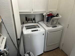 Washroom with a textured wall, cabinet space, washing machine and dryer, and dark tile patterned floors