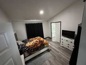 Bedroom with wood finished floors, ensuite bath, and lofted ceiling