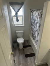Full bath with light wood-type flooring, a textured wall, and shower / tub combo with curtain