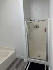 Full bathroom featuring wood finished floors, a bath, a stall shower, and a textured wall