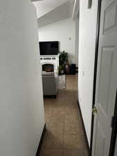 Hallway with a textured wall, dark tile patterned flooring, a textured ceiling, and vaulted ceiling