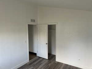 Unfurnished bedroom with dark wood finished floors, vaulted ceiling, and a closet