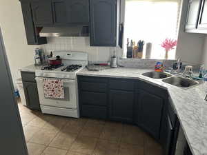 Kitchen featuring white gas range oven, light countertops, tasteful backsplash, and wall chimney range hood