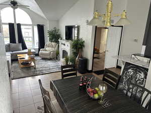 Dining room featuring light tile patterned floors, lofted ceiling, a fireplace, and a ceiling fan
