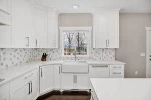 Kitchen with white cabinets, light stone countertops, with farm sink, tasteful backsplash, and dark wood-style floors
