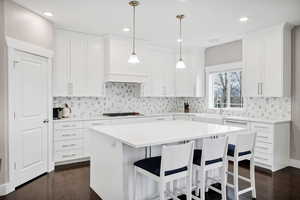 Kitchen with a kitchen breakfast bar, dark wood-style floors, hanging light fixtures, a center island, and white cabinetry
