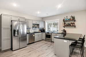 Full Kitchen featuring open shelves, appliances with stainless steel finishes, decorative backsplash, a peninsula, and light wood-type flooring
