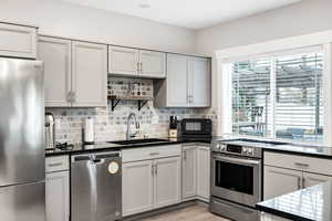 Kitchen with appliances with stainless steel finishes, decorative backsplash, dark stone countertops, and light wood-type flooring