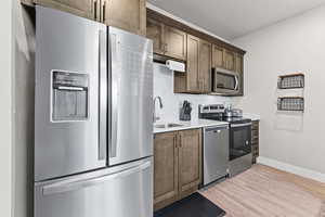 Kitchen featuring appliances with stainless steel finishes, light wood-style floors, tasteful backsplash, dark brown cabinetry, and a textured ceiling