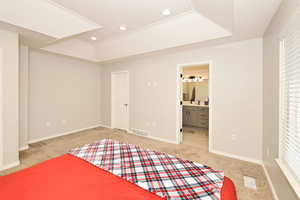 Unfurnished bedroom with a tray ceiling, recessed lighting, light carpet, and ensuite bath