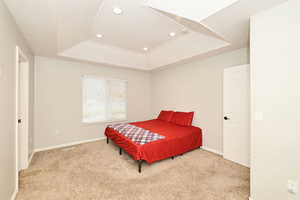 Bedroom with a raised ceiling, light carpet, and recessed lighting