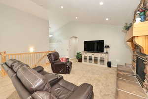 Living room featuring arched walkways, light carpet, a fireplace, high vaulted ceiling, and recessed lighting