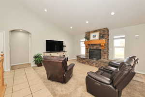 Living area with light carpet, arched walkways, vaulted ceiling, a stone fireplace, and recessed lighting