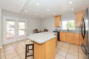 Kitchen with a center island, black appliances, light stone counters, light tile patterned floors, and recessed lighting