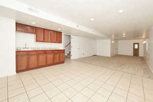 Kitchen featuring brown cabinetry, tile countertops, light colored carpet, light tile patterned floors, and open floor plan